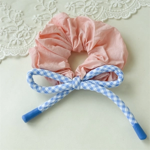 Détail d'un chouchou rose avec ruban à carreaux bleus sur fond de dentelle blanche