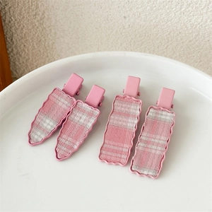 Detail view of pink plaid fabric hair clips in a ceramic tray on a textured background