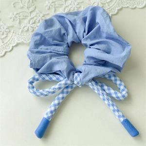 Détail d'un chouchou bleu clair avec nœud à carreaux vichy sur un fond crème élégant
