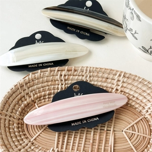 Three acetate hair clips in pink and white marble textures on a woven tray setting