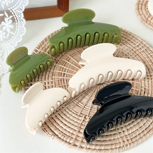 Glossy shell-shaped hair claw clips in olive green, cream and black on woven mat
