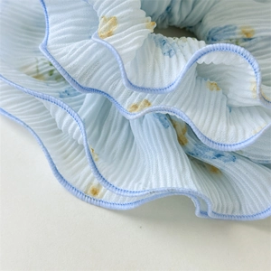 Detail of light blue floral scrunchie featuring pleated chiffon fabric and wavy edges