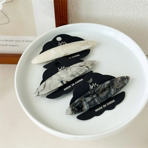 Three acetate hair clips in marble texture patterns placed on a ceramic tray