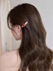Brown amber-textured acetate oval hair clip shown worn on wavy hair side profile
