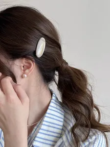Close-up of a cream marbled acetate oval hair clip and pearl earring on a model