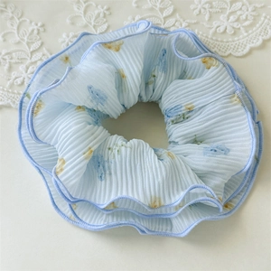 Detailed close-up of light blue floral scrunchie with layered chiffon and pleated texture