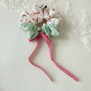 Detail of cherry print scrunchie with a red plaid bow and green fabric patchwork