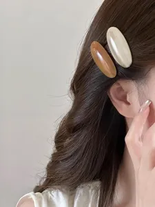 Detail showing amber and ivory acetate oval hair clips worn on the side hair
