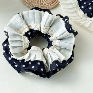 Detail eines dunkelblauen Polka-Dot-Scrunchies mit weißen Falten-Spitzenkanten und Stofftextur