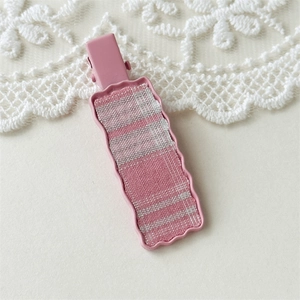 Detail of pink plaid fabric inlay on a wavy metal hair clip with a soft lace background