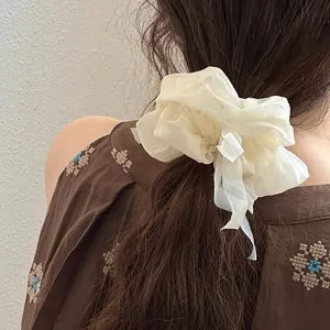 Detail showing an oversized cream puff-纱 hair tie worn in a low ponytail style