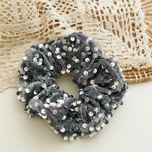 Close-up of a grey velvet scrunchie with silver sequins on a lace and rattan background