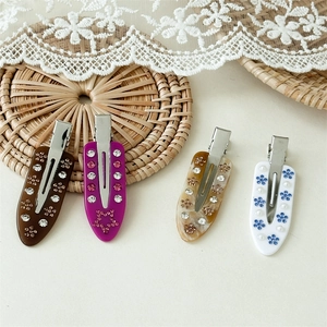 Detail view of acetate duckbill hair clips with marble texture and rhinestone flowers