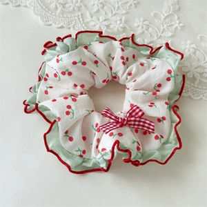 Detail of sweet cherry scrunchie with red plaid bow and green ruffled edges