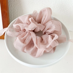 Close-up of a light pink pleated chiffon scrunchie with delicate decorative ribbons