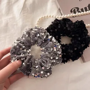 Detailed shot of sequin velvet hair scrunchies in black and grey on a white fabric