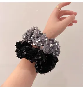 Detailed view of sequin scrunchies in black and grey velvet with shimmering circular patterns