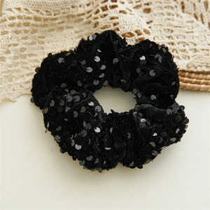 Detail of black sequined hair scrunchie with sparkling texture on soft velvet fabric
