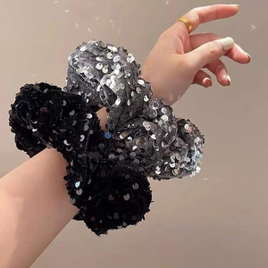 Close-up of black and silver sequined scrunchies worn on a wrist with glowing light spots