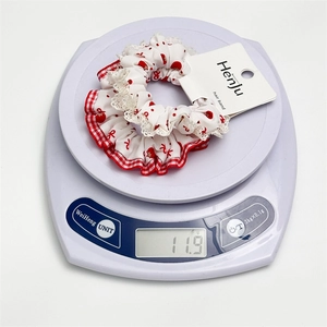 Polka dot heart scrunchie with lace trim and red plaid ruffles on a white scale
