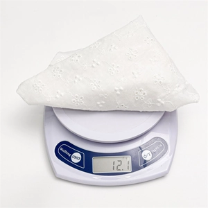 Detailed view of white floral lace triangle scarf weighing 12.1g on a digital scale