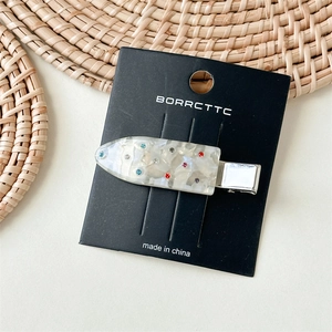 Detail of a pearlescent white duckbill hair clip with colorful rhinestones on a card