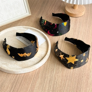 Close-up of three wide headbands with golden bat and star patterns on smooth black satin