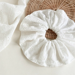 Detailed close-up of white broderie anglaise lace scrunchie with floral embroidery