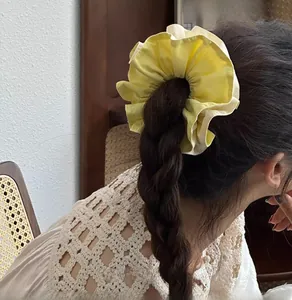 Detailed view of yellow and beige oversized scrunchie styled on a dark braided hairstyle