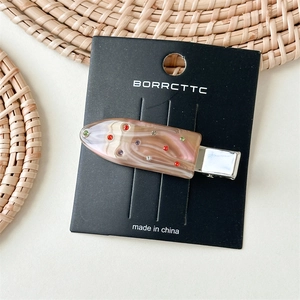 Detailed view of marble resin hair clip with colorful rhinestones on card display
