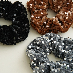 Detailed texture of sequined velvet scrunchies in black, caramel brown, and silver grey