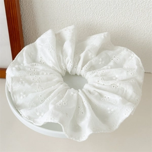 Detail of white lace hair scrunchie with hollow floral embroidery on a ceramic plate