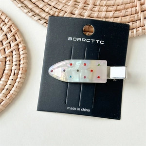 Detail of a pearlescent white acrylic hair clip with colorful rhinestones on a card