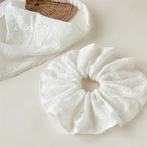 Detailed macro view of white lace floral embroidery on hair scrunchie and headband set