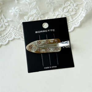 Detail of marble acetate hair clip with pink floral rhinestones on white lace background
