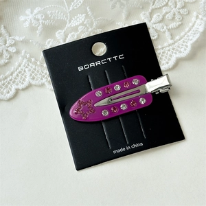 Detailed shot of purple acetate hair clip with pink and white rhinestones on lace background