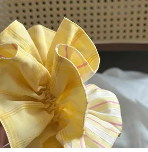 Detail of yellow and pink striped gingham scrunchie on a woven rattan background