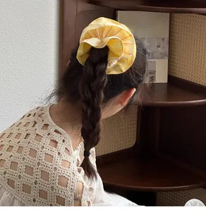 Detail of yellow checkered scrunchie styled on a side braid for a chic hair look