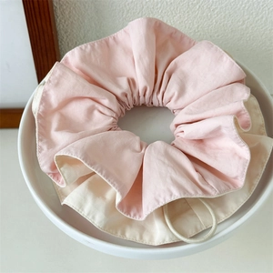 Macro detail of large ruffled dual-tone pink and beige scrunchie in a white ceramic bowl