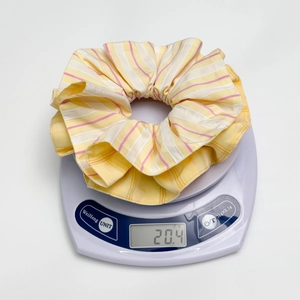 Detailed close-up of a large yellow striped fabric scrunchie weighing 20.4g on a scale