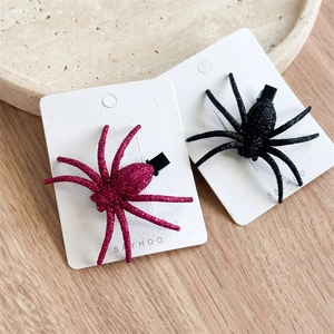 Detailed shot of purple and black glitter spider hair clips on a white display card
