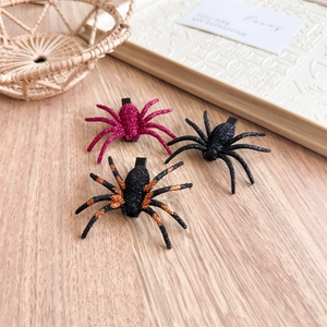 Close-up of three glittery Halloween spider hair clips on a minimalist wooden surface