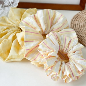 Detailed close-up of three yellow striped and checkered fabric hair scrunchies on a lace mat