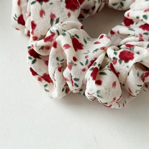 Détail du chouchou crème avec motifs floraux rouges et texture de tissu plissé