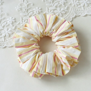 Detail of yellow and white striped fabric scrunchie with pink lines on lace background