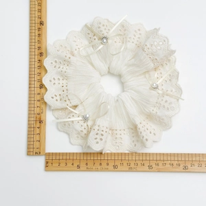 Large white lace scrunchie with bows and pearls measured by wooden rulers on white background