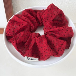 Detail of red polka dot oversized hair scrunchie with brand tag on ceramic plate