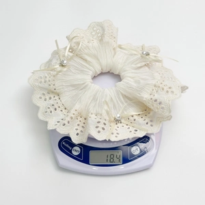 Detail shot of a beige lace hair scrunchie with satin bows and pearls on a scale