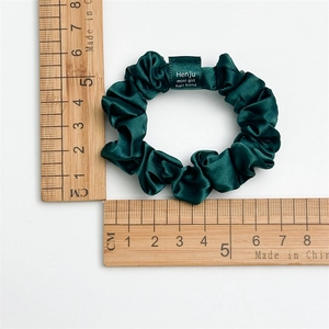 Makro-Detail eines dunkelgrünen Satin-Haargummis mit gewebtem Etikett und 5,5cm Durchmesser