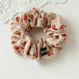 Détail d'un chouchou en tissu floral avec des roses rouges sur fond beige et étiquette